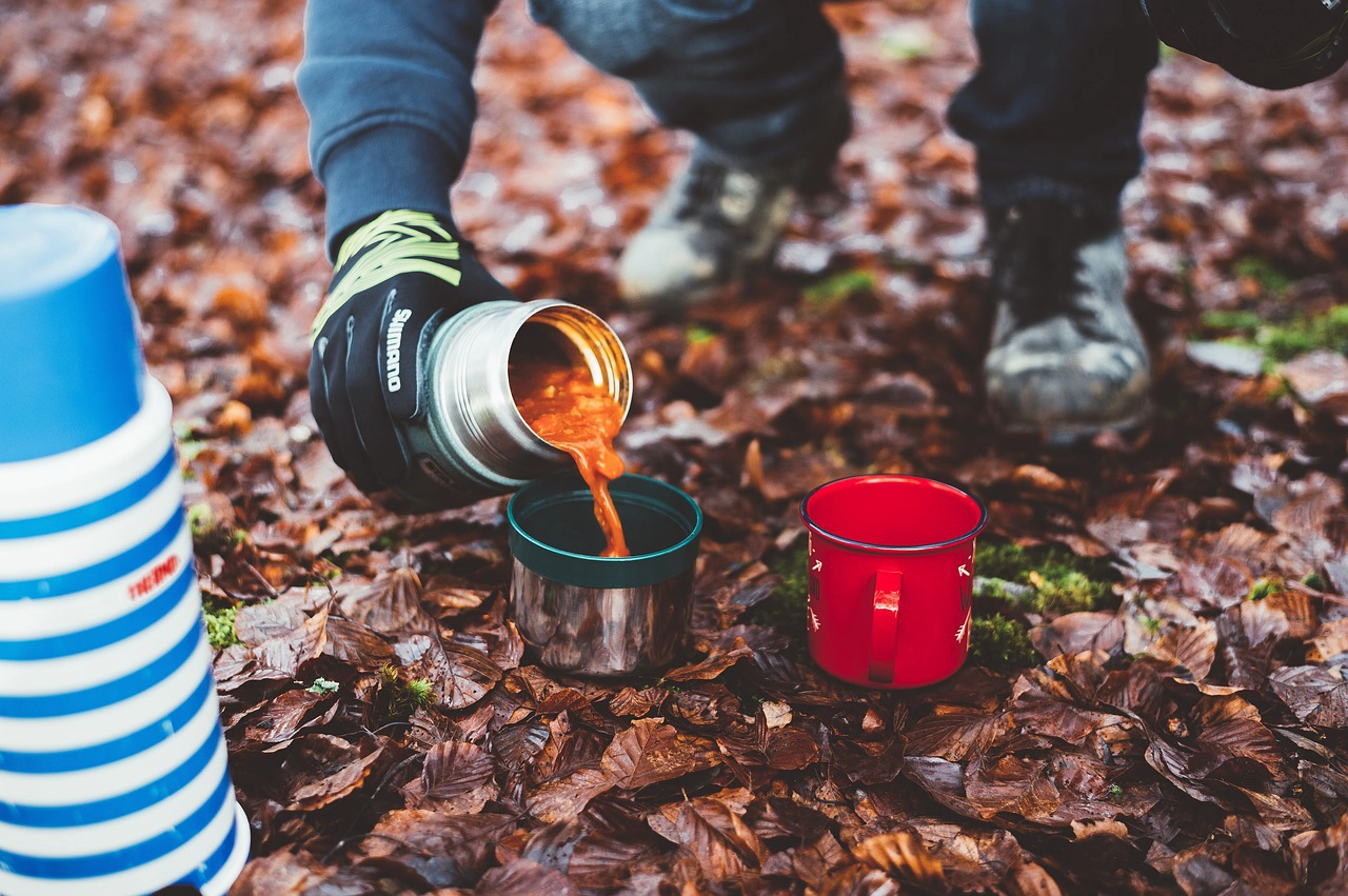 Person pouring soup from a thermos while camping