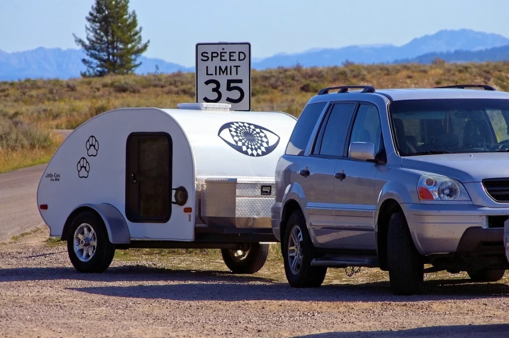 Car towing a teardrop travel trailer on a desert road